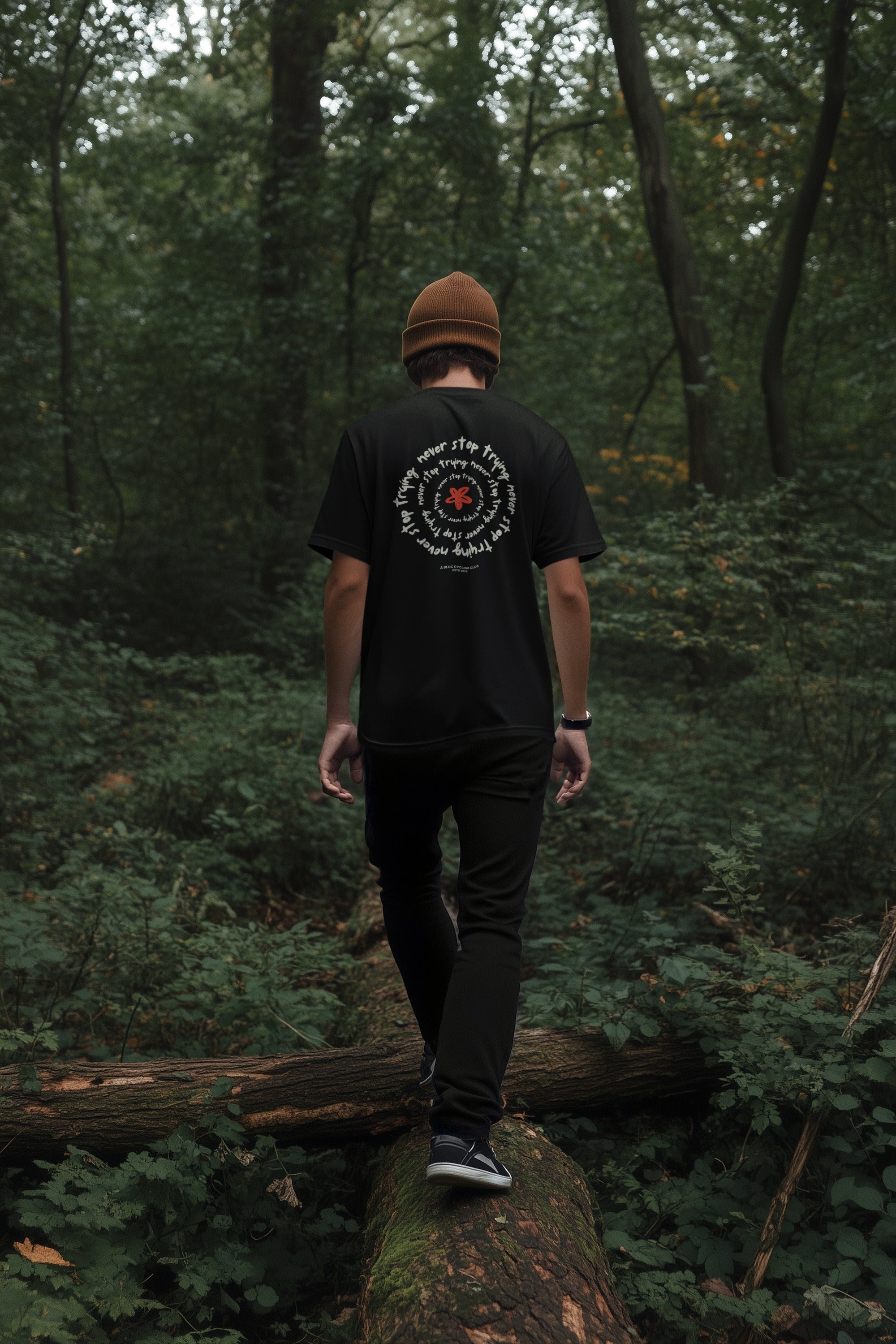 Person walking on a log in a forest wearing a black t-shirt with a logo.